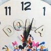 alt="Enfant heureux pointant son prénom sur l'horloge murale colorée dans sa chambre"